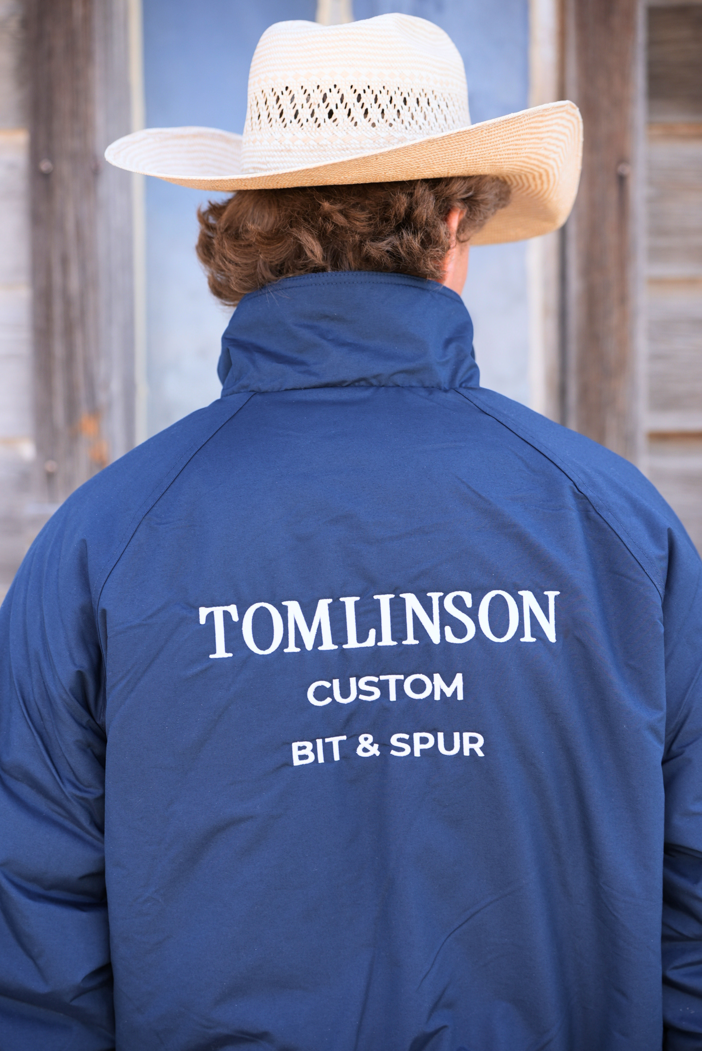 Person wearing a blue jacket with 'Tomlinson Custom Bit & Spur' text, facing away from the camera.