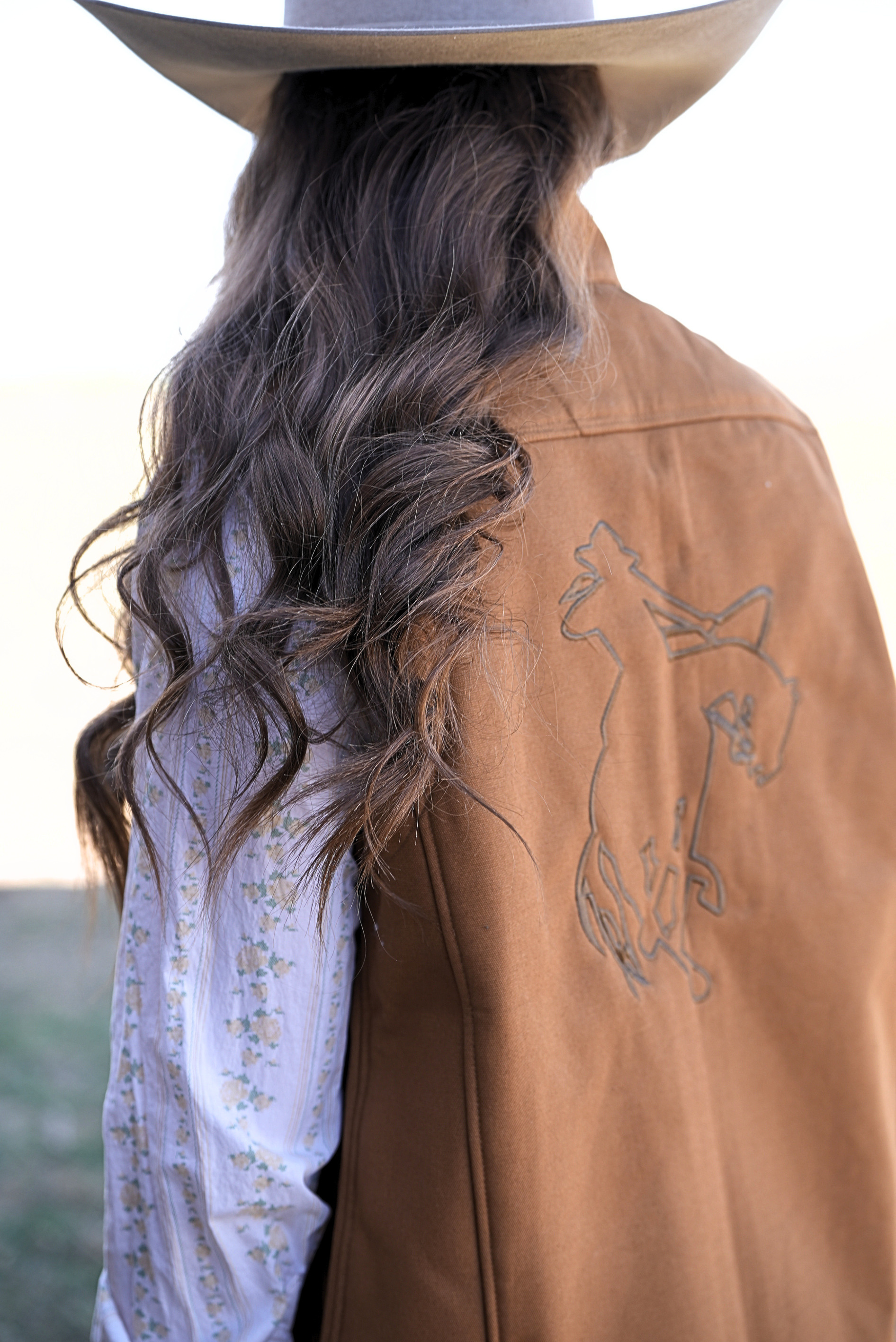 Woman wearing a brown vest featuring an embroidered cowboy on the back.