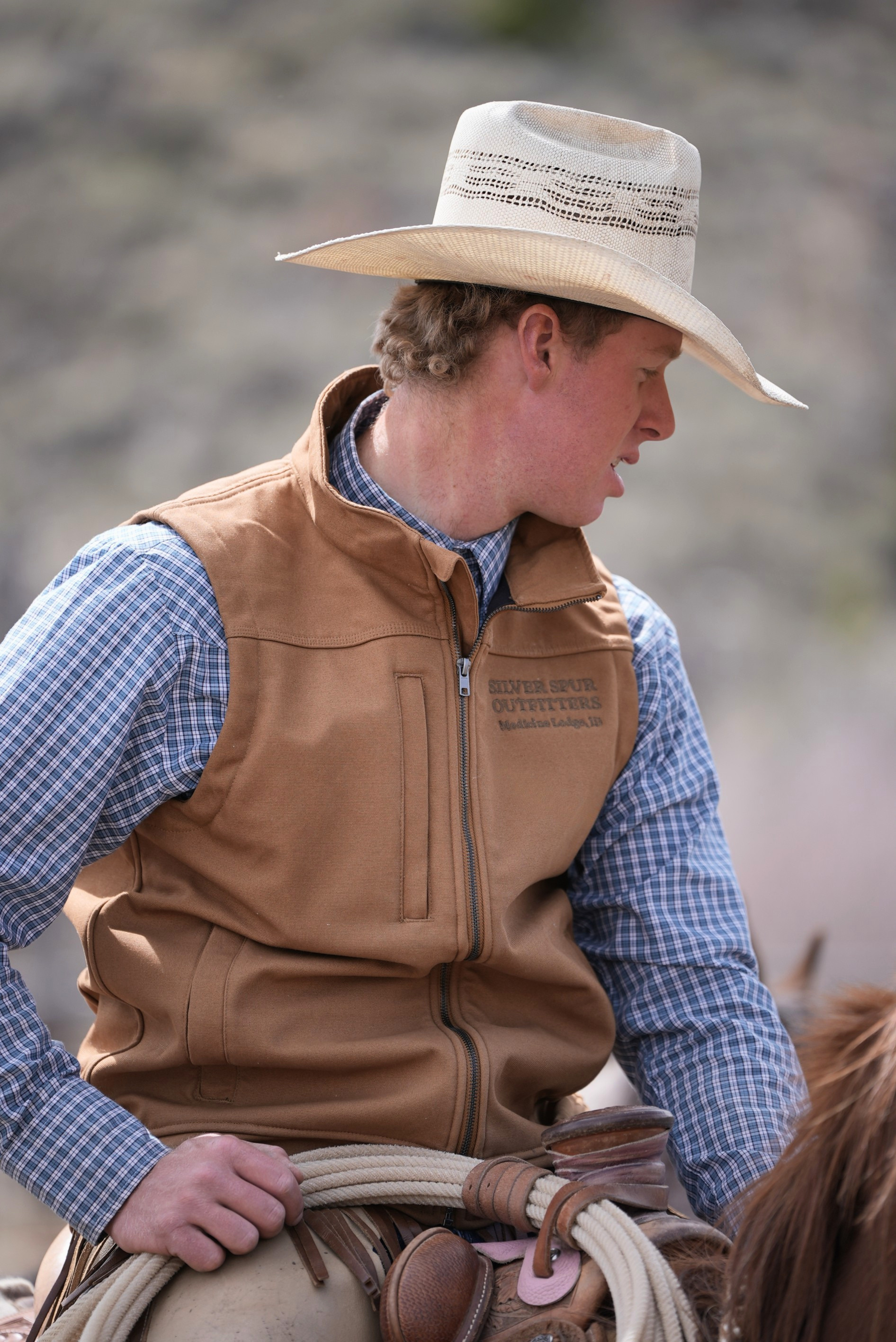 Man in cowboy hat and vest sitting on a horse with a blurred natural background