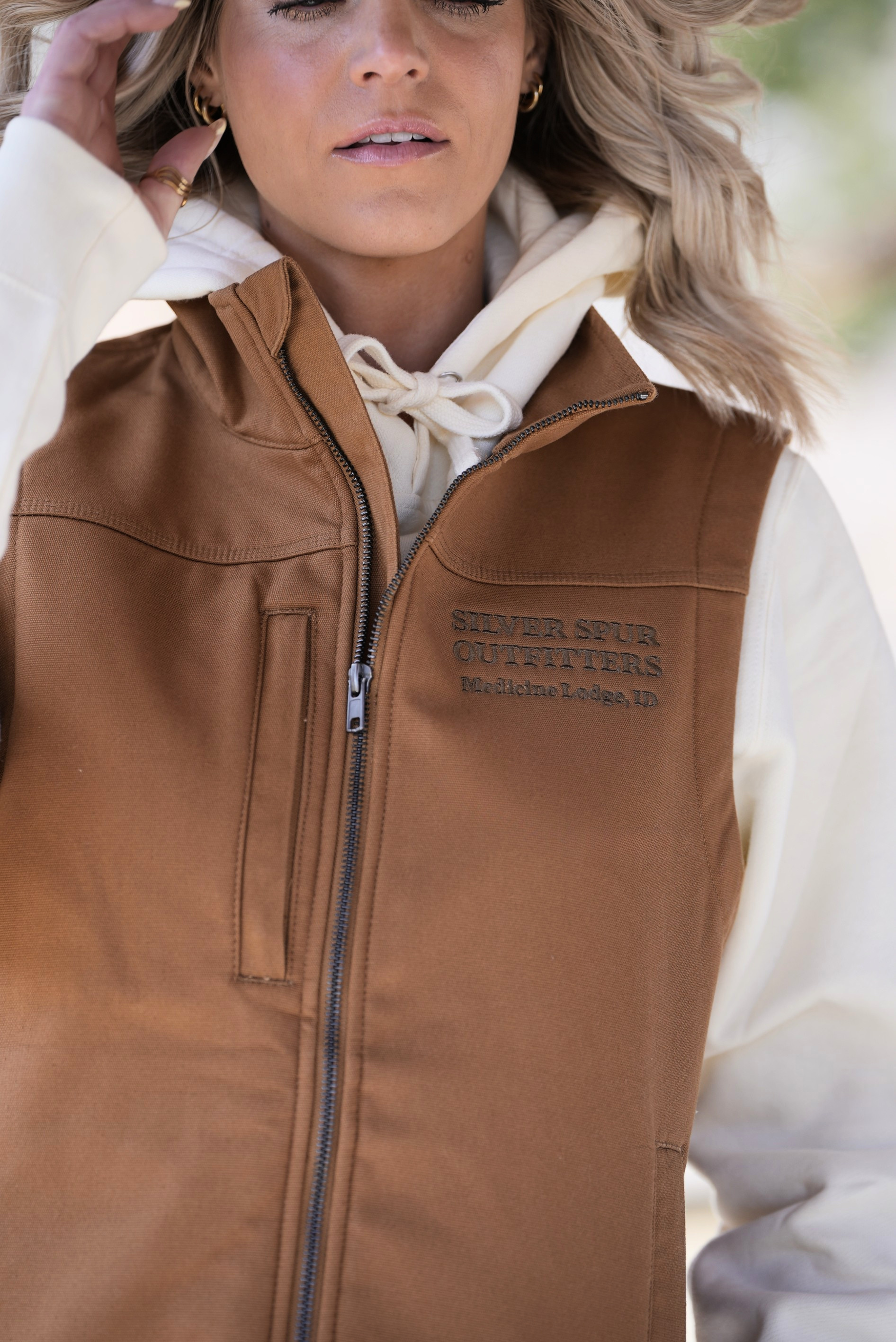 Brown vest with a brand logo worn by a person, blurred background