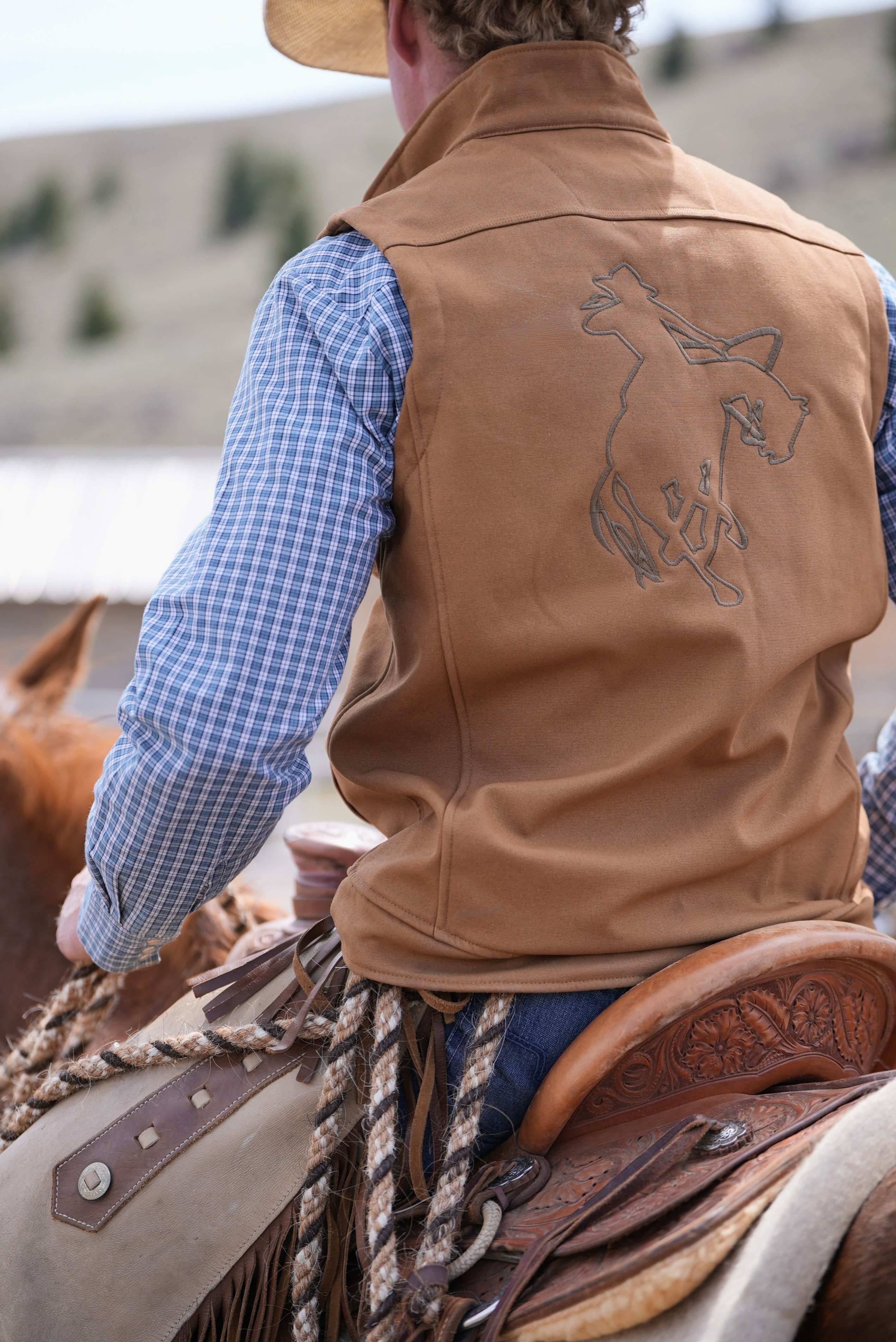 Person wearing a brown leather vest with a horse design, sitting on a horse.