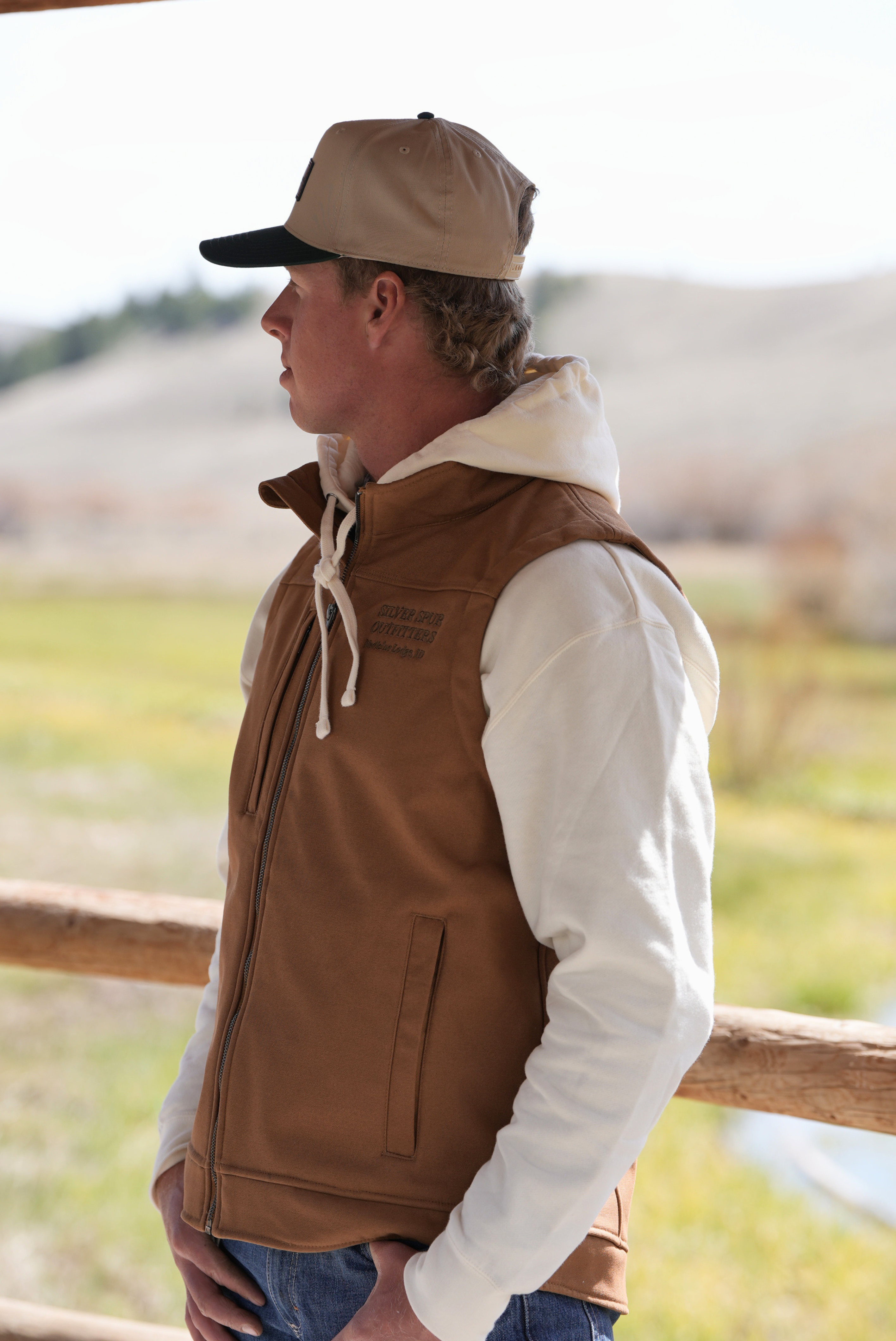 Man wearing a brown vest and cap in a natural setting