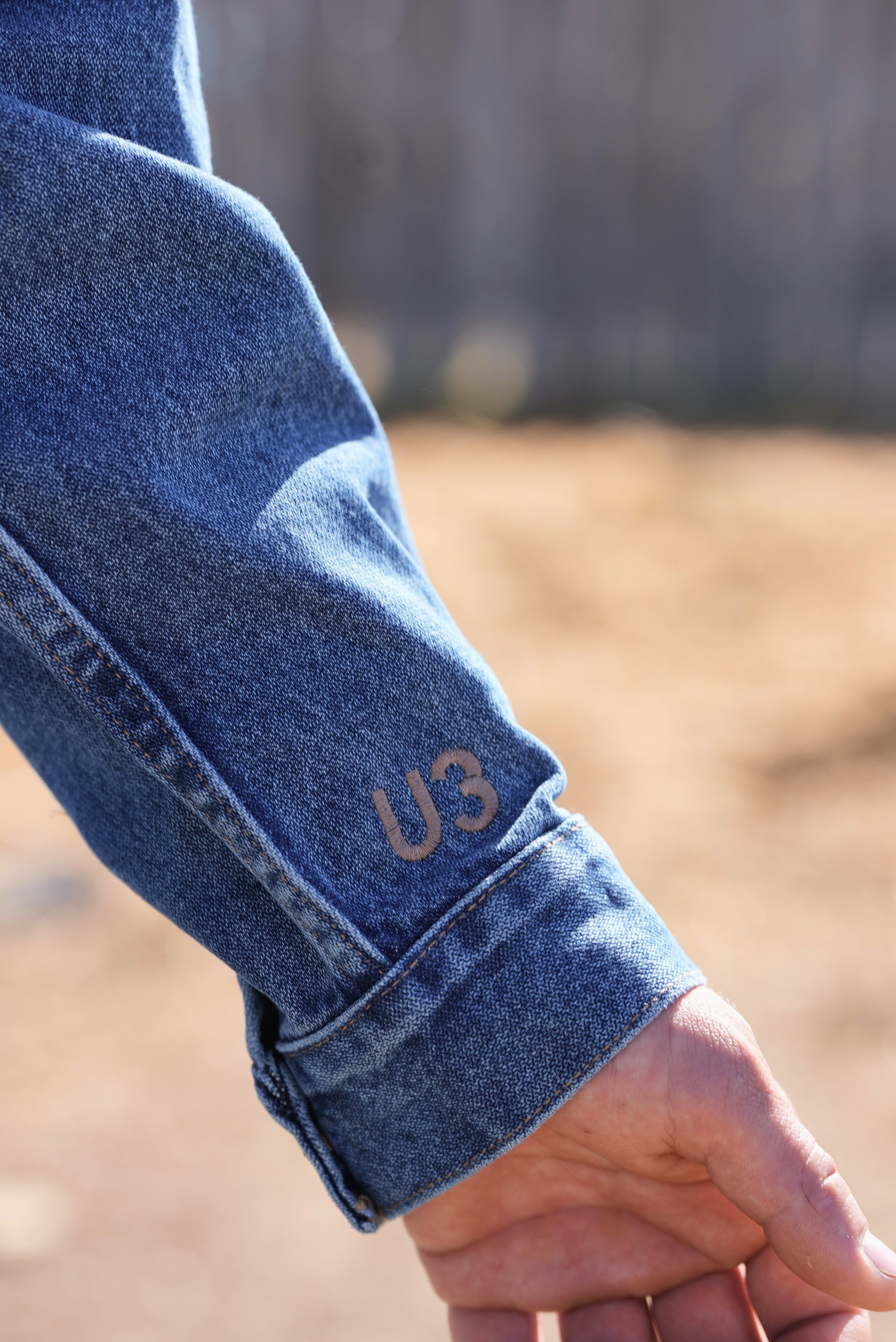 Close-up of a person wearing blue jeans with 'U3' branding on the cuff, against a blurred natural background.