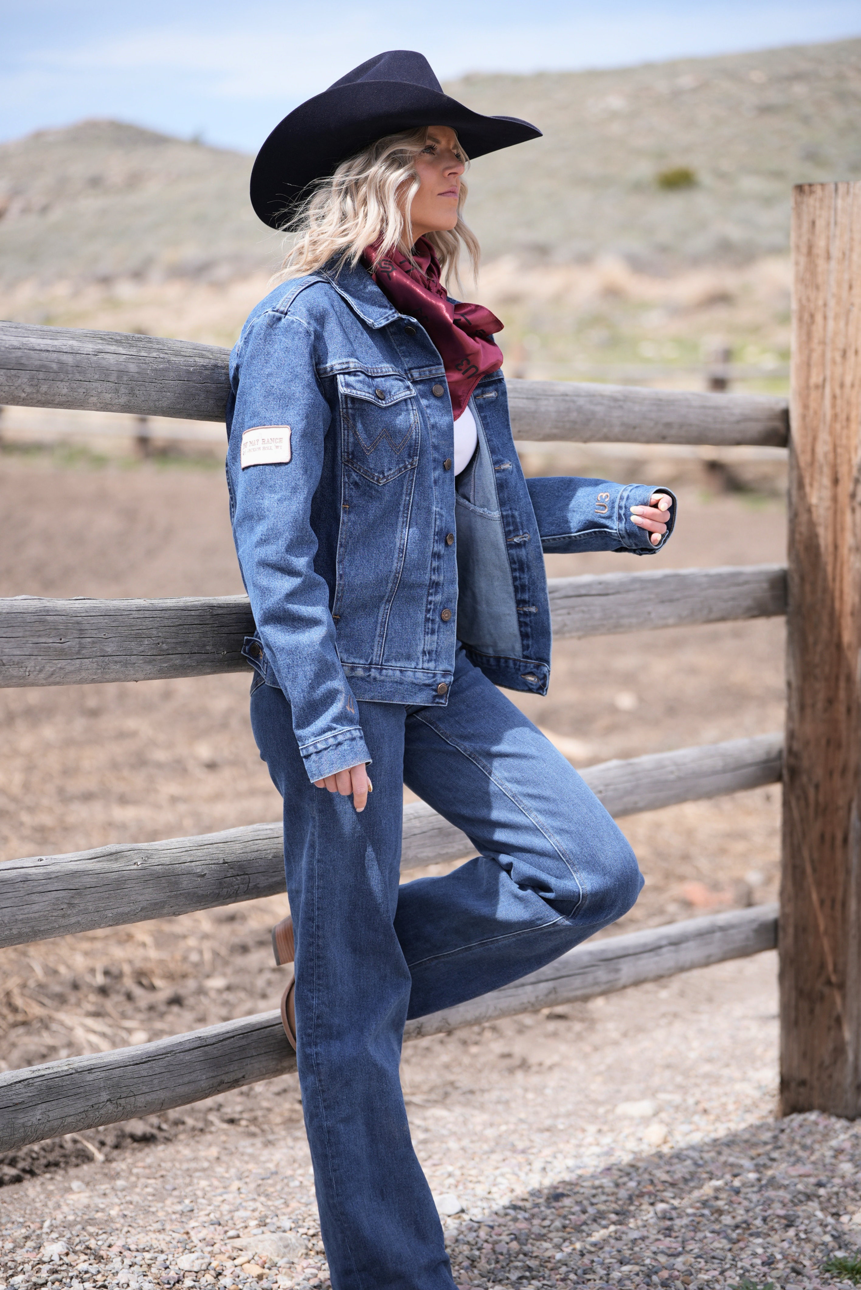 Person wearing a denim jacket and jeans standing near a wooden fence in an outdoor setting.