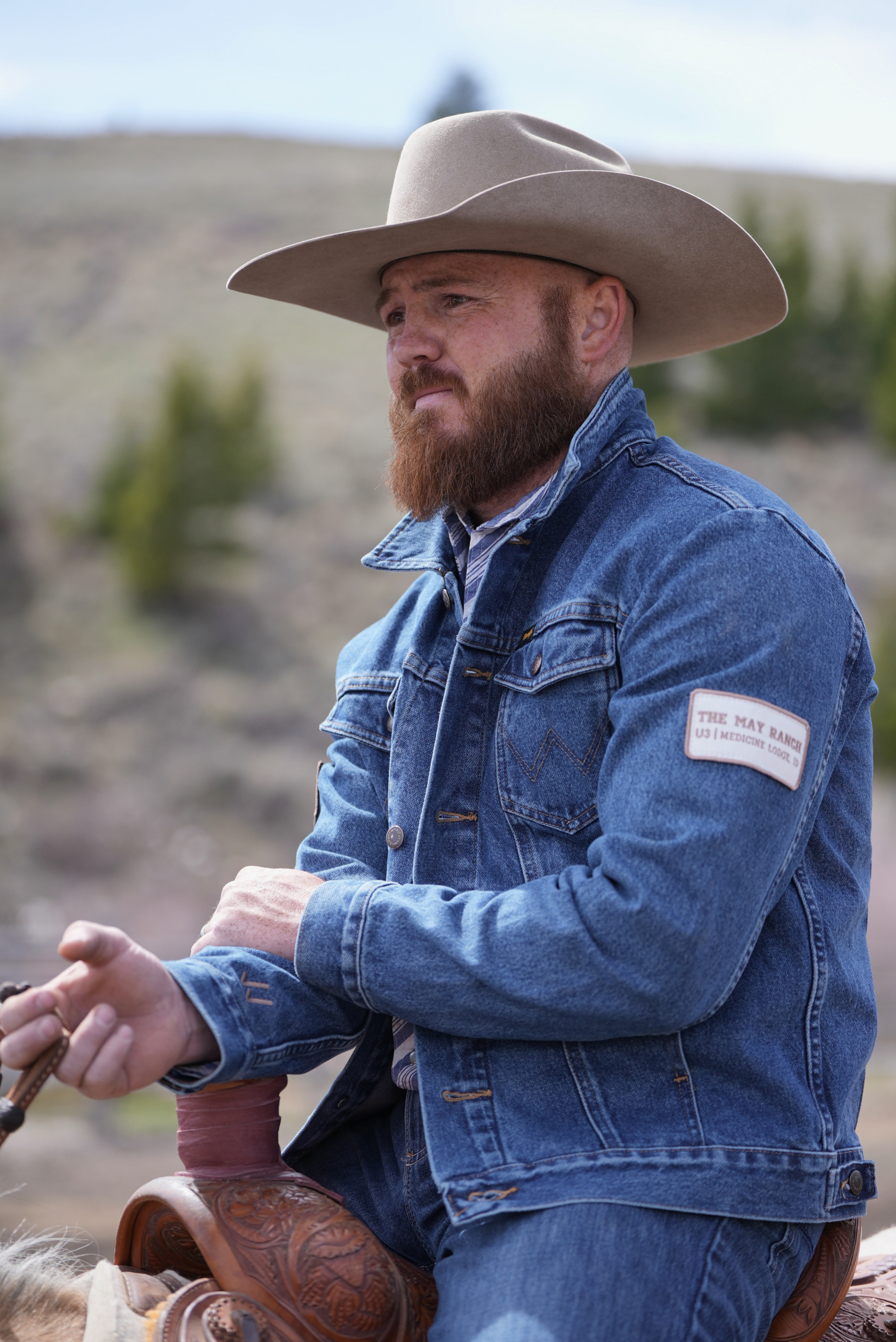 Man wearing a blue denim jacket and cowboy hat in a Western setting.
