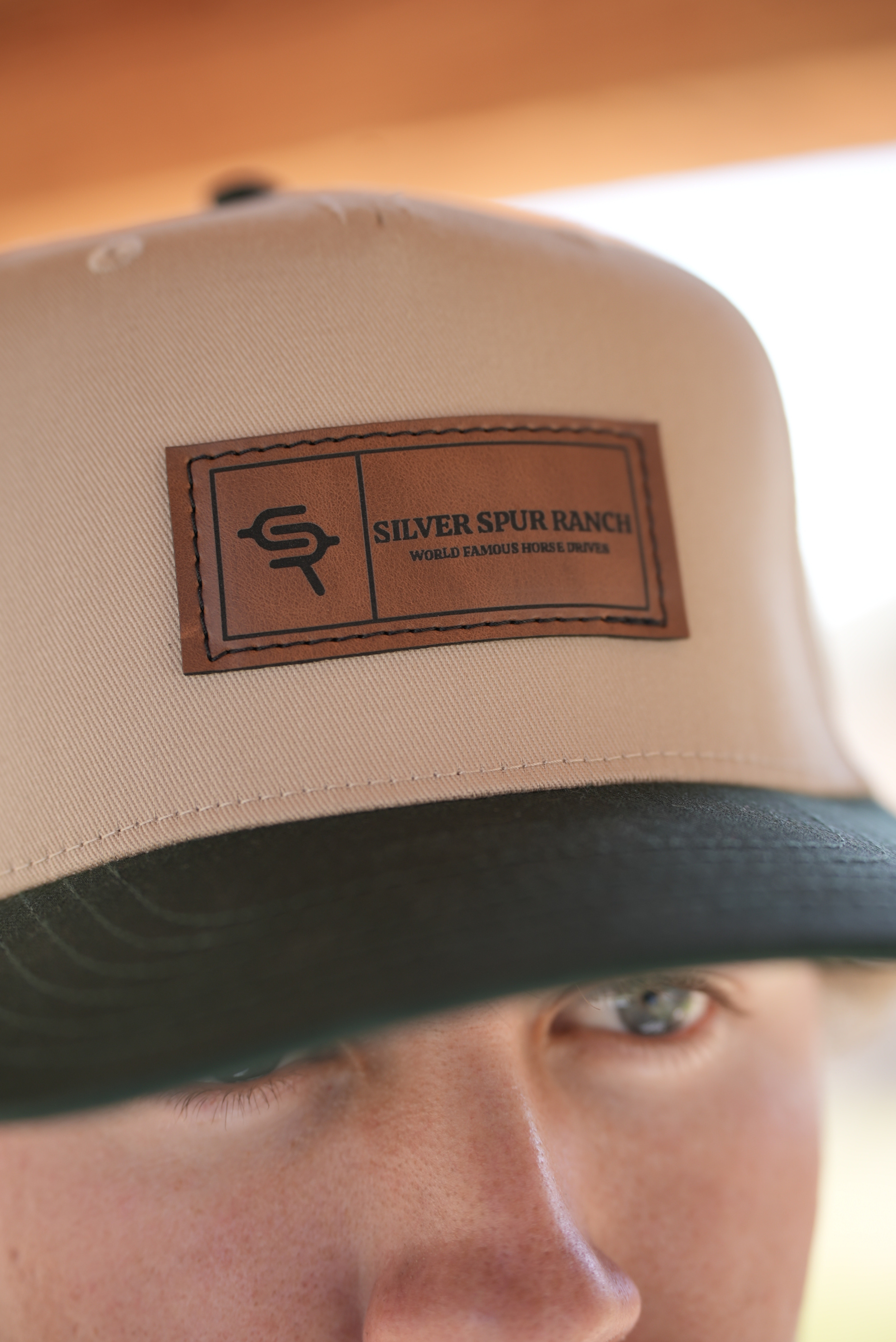 Beige and green two tone cap with a leather patch featuring 'Silver Spur Ranch' logo.