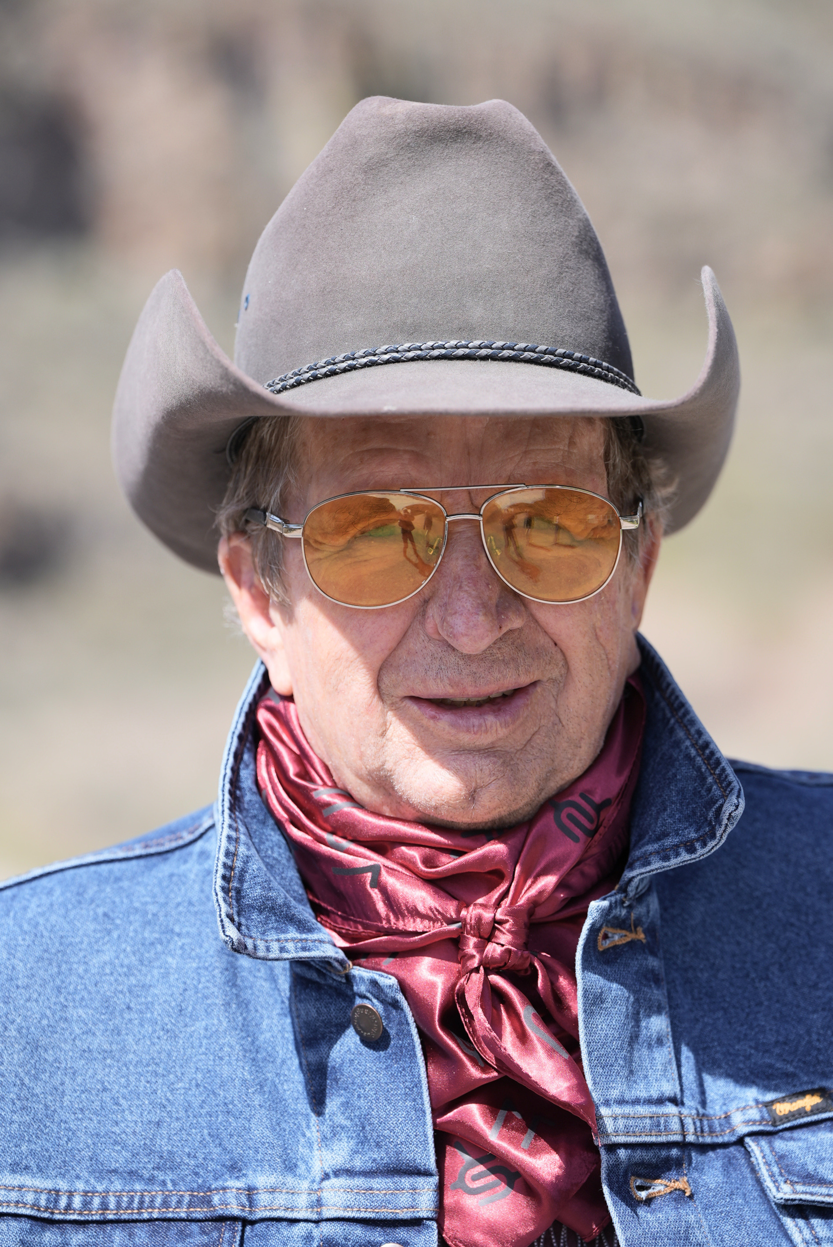 Man wearing a cowboy hat, sunglasses, and a red silk cowboy wild rag featuring several different brands.